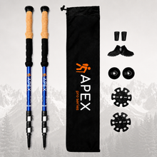 Load image into Gallery viewer, A pair of blue APEX Pro Series hiking poles with cork and tan grips, shown alongside a black drawstring bag, shoe covers, toe pads, and buckle accessories on a light gray background with a faint mountain silhouette.