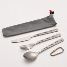 Load image into Gallery viewer, A 3-piece titanium camping utensil set by APEX, including a knife, fork, spoon, and a carabiner, arranged diagonally next to a gray drawstring pouch with a red toggle on a light gray background.

