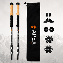 Load image into Gallery viewer, A pair of black APEX Pro Series hiking poles with cork and tan grips, shown alongside a black drawstring bag, shoe covers, toe pads, and buckle accessories on a light gray background with a faint mountain silhouette.
