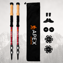 Load image into Gallery viewer, A pair of red APEX Pro Series hiking poles with cork and tan grips, shown alongside a black drawstring bag, shoe covers, toe pads, and buckle accessories on a light gray background with a faint mountain silhouette.
